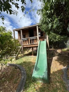 Large wooden cubby house on stilts with slide